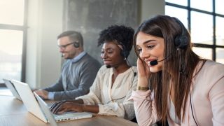 Customer service executive working at office. Colleagues working in a call center. Beautiful business people in headsets are using computers and smiling while working in office.